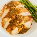 Medallions of sautéed chicken breasts with mustard pan sauce and asparagus in a white bowl.