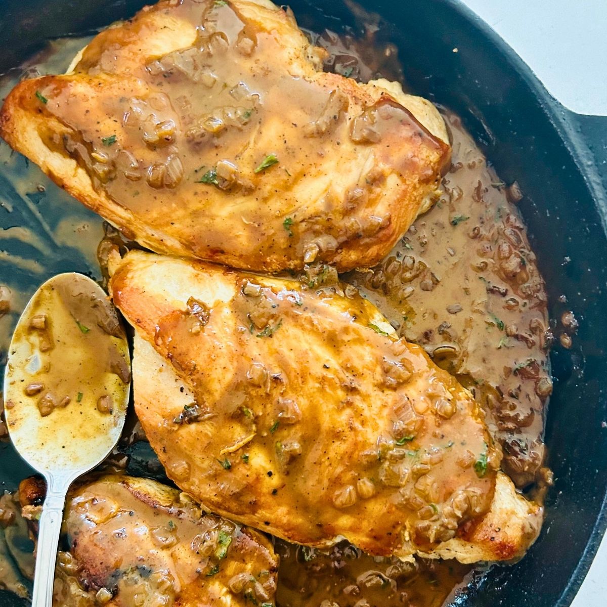 Sautéed chicken breasts with Dijon mustard pan sauce spooned over them in a cast-iron skillet.