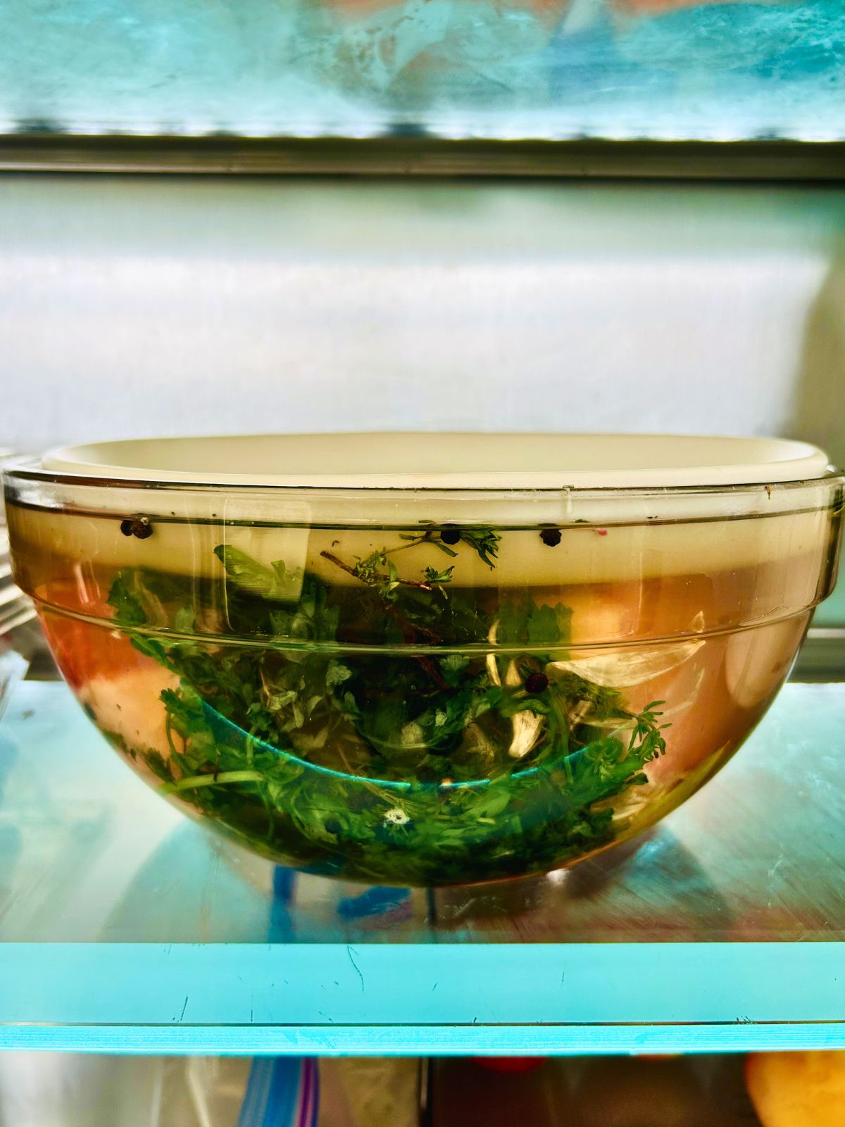 A bowl with pork rib roast soaking in a herb brine on the shelf of the refrigerator.