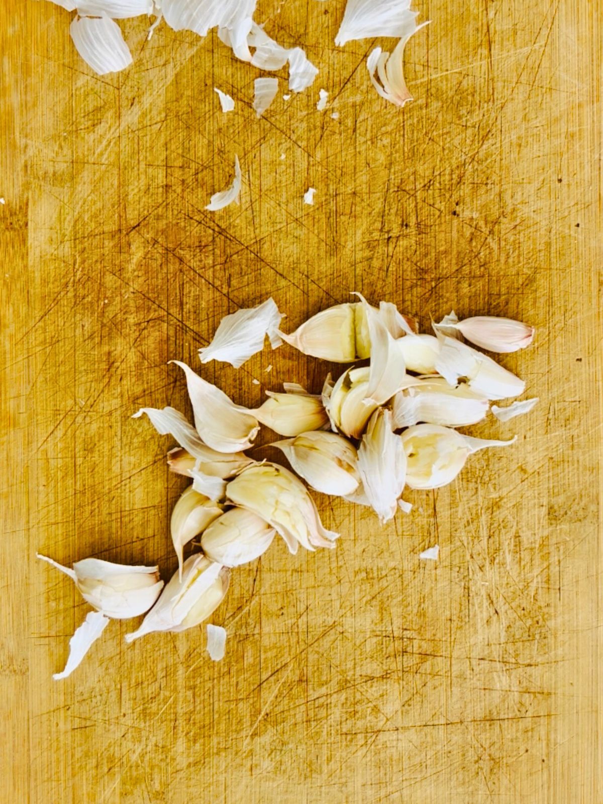 Whole garlic cloves crushed on a cutting board.