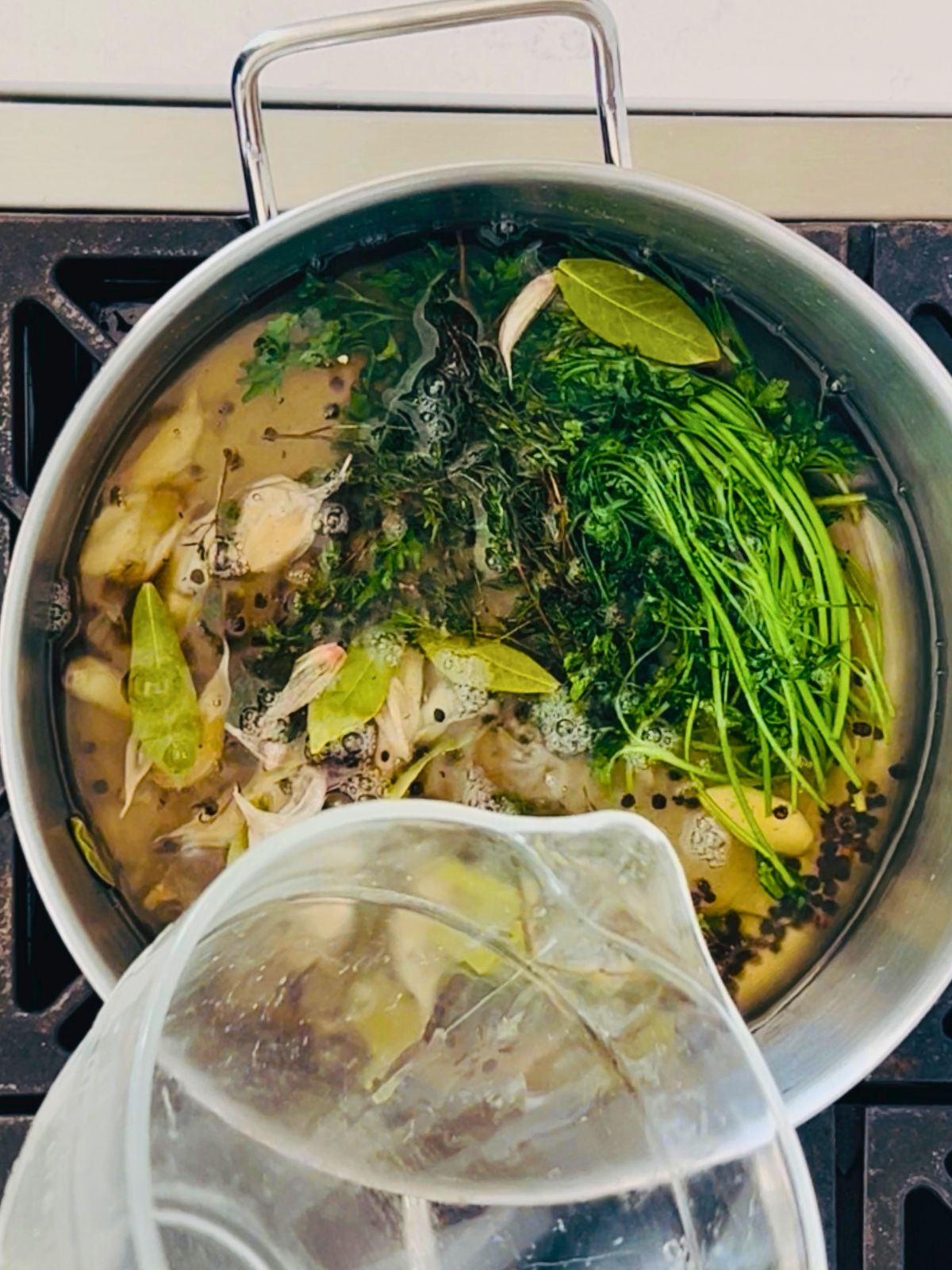 Cold water is poured into the simmering pot of garlic, herbs, peppercorns, salt, and sugar.