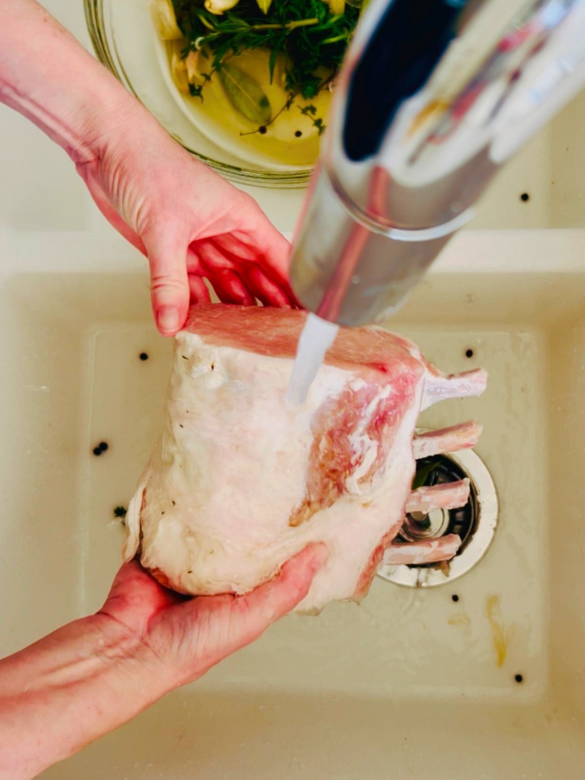 The brined pork rib roast is getting rinsed with cold water in the sink.