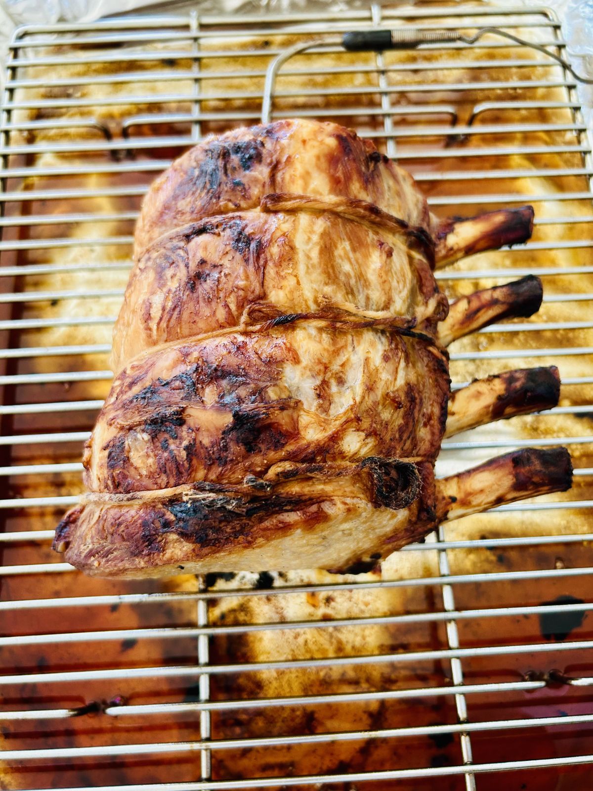 Herb and garlic brined pork rib roast finished cooking and resting on a wire rack over a rimmed sheet pan.
