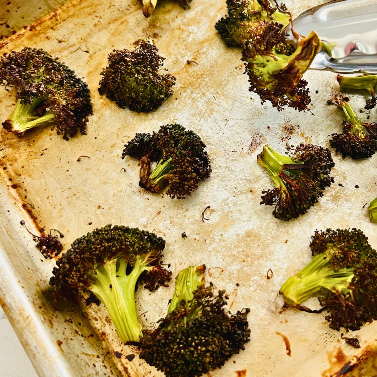 Overcooked roasted broccoli florets on a sheet pan.