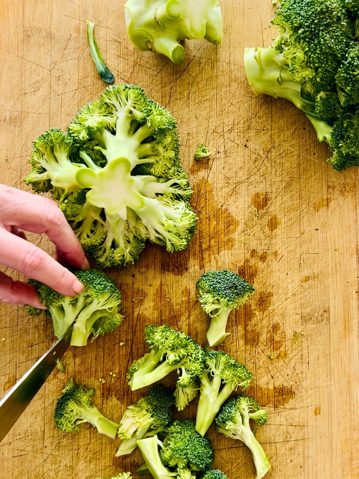 A crown of broccoli is trimmed with a chef's knife into 2-inch chunks.