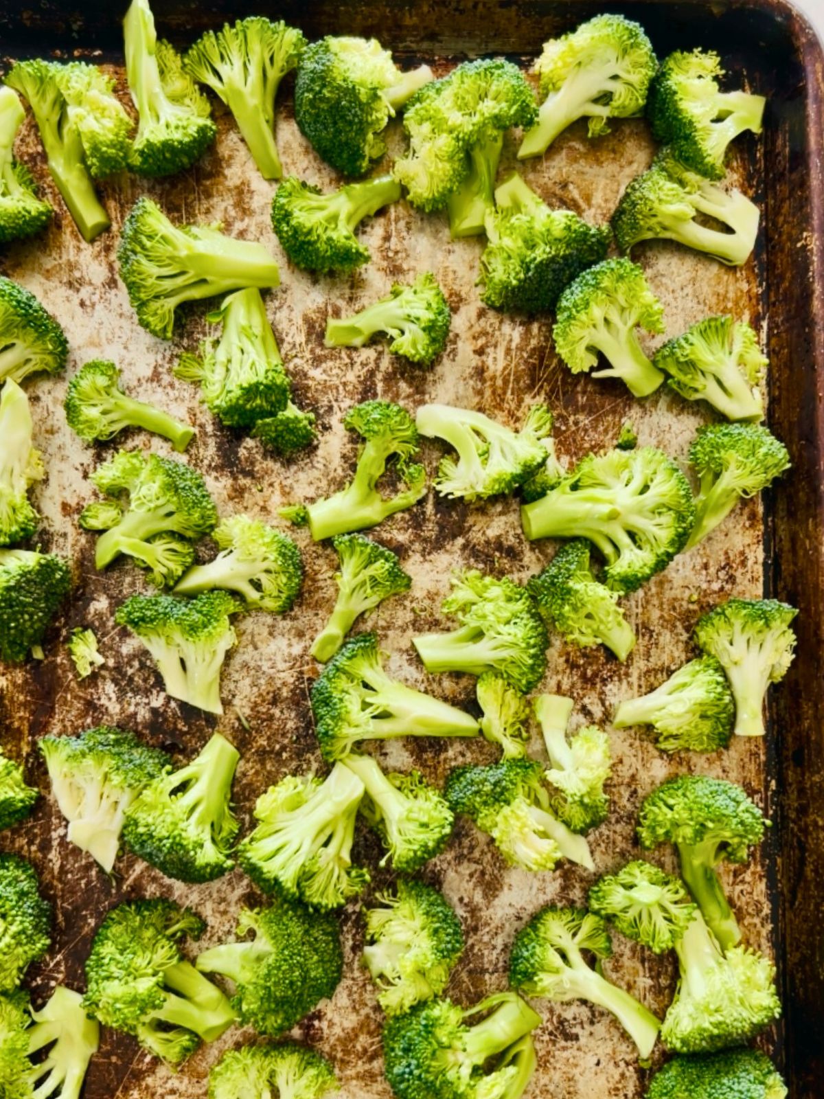 A cookie sheet with chunks of broccoli spaced out and ready to roast.