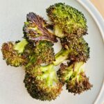 Crispy roasted broccoli resting on a white plate.