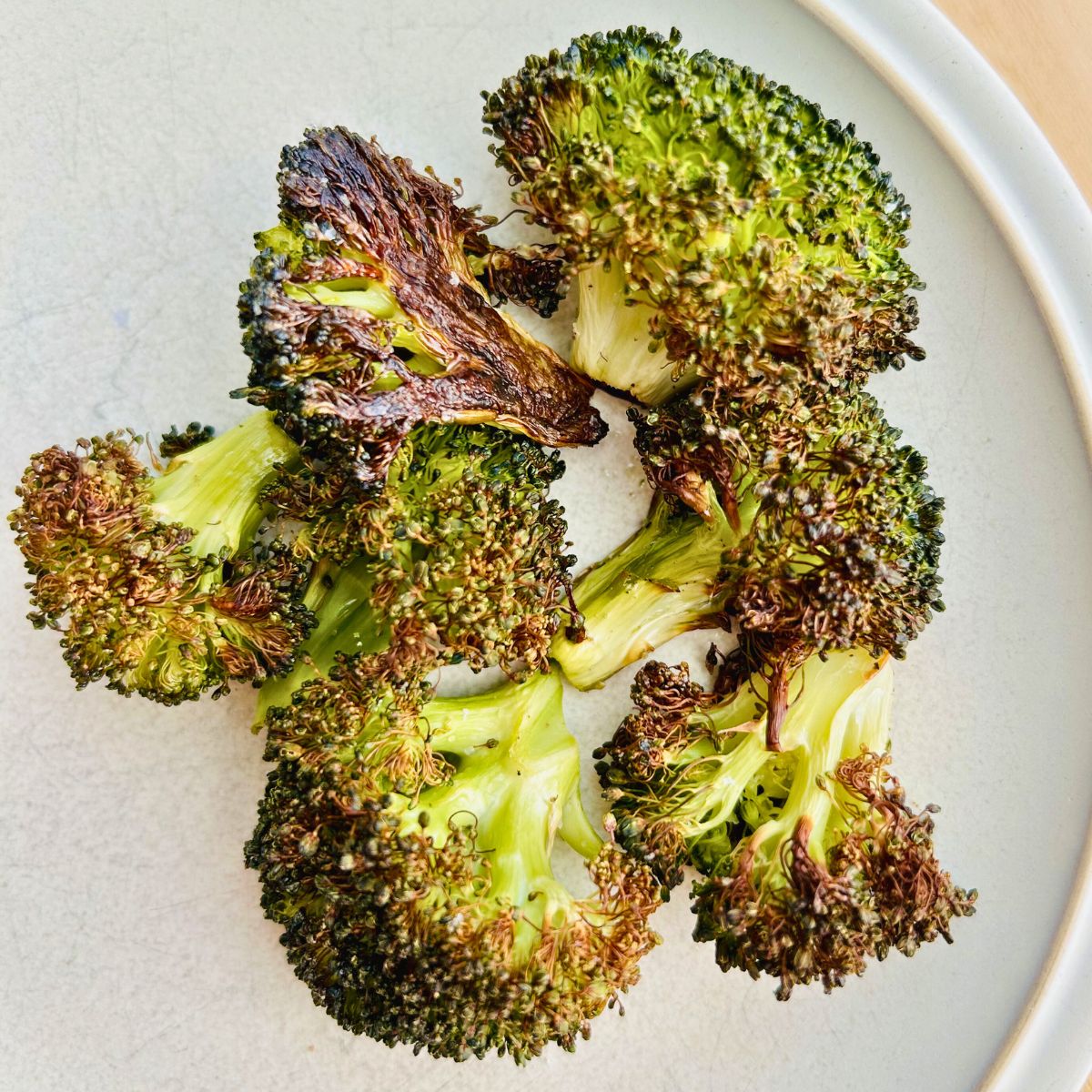 Crispy roasted broccoli resting on a white plate.