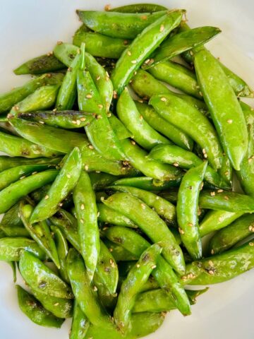 Sautéed sugar snap peas with sesame oil and sesame seeds in a white bowl.