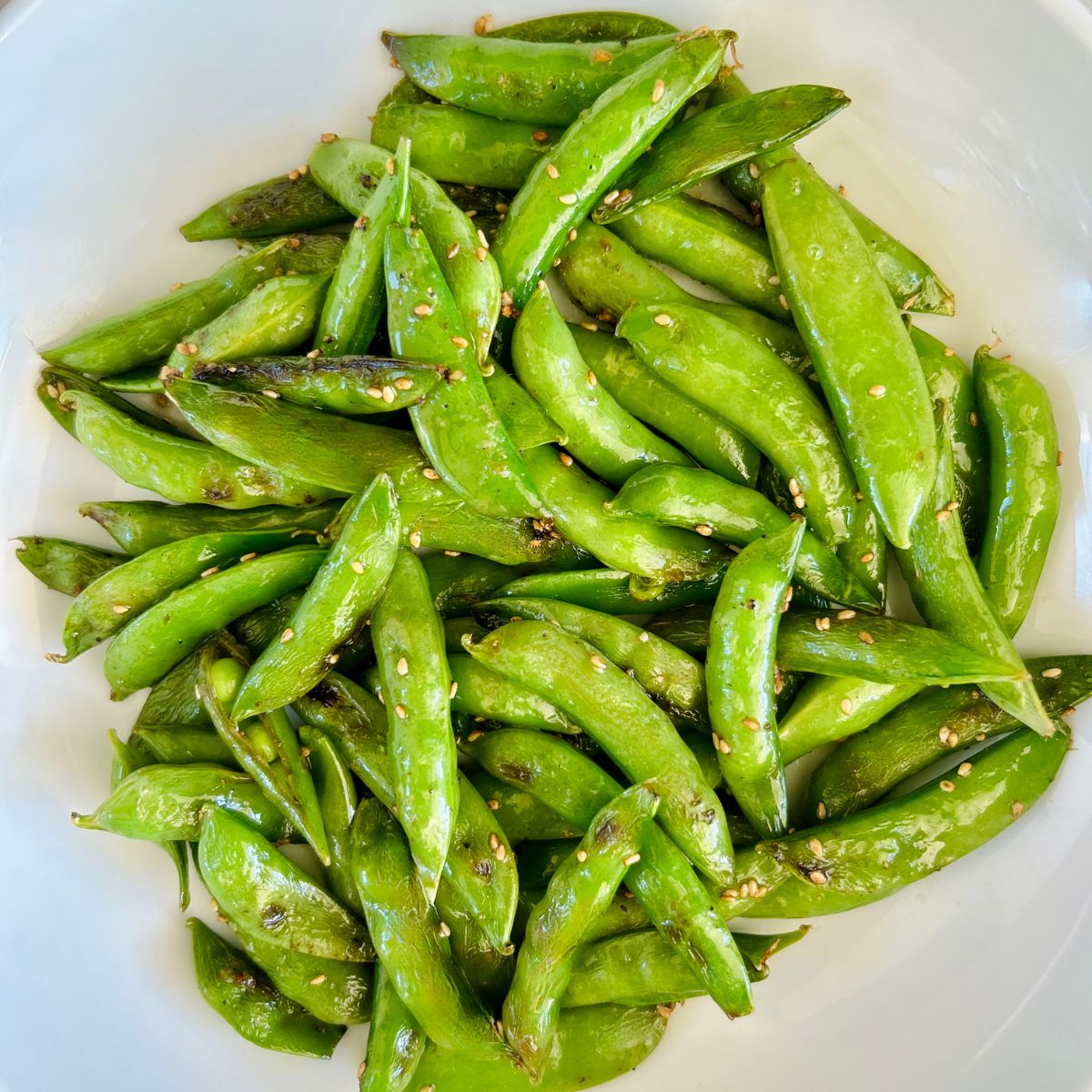 Sautéed sugar snap peas with sesame oil and sesame seeds in a white bowl.