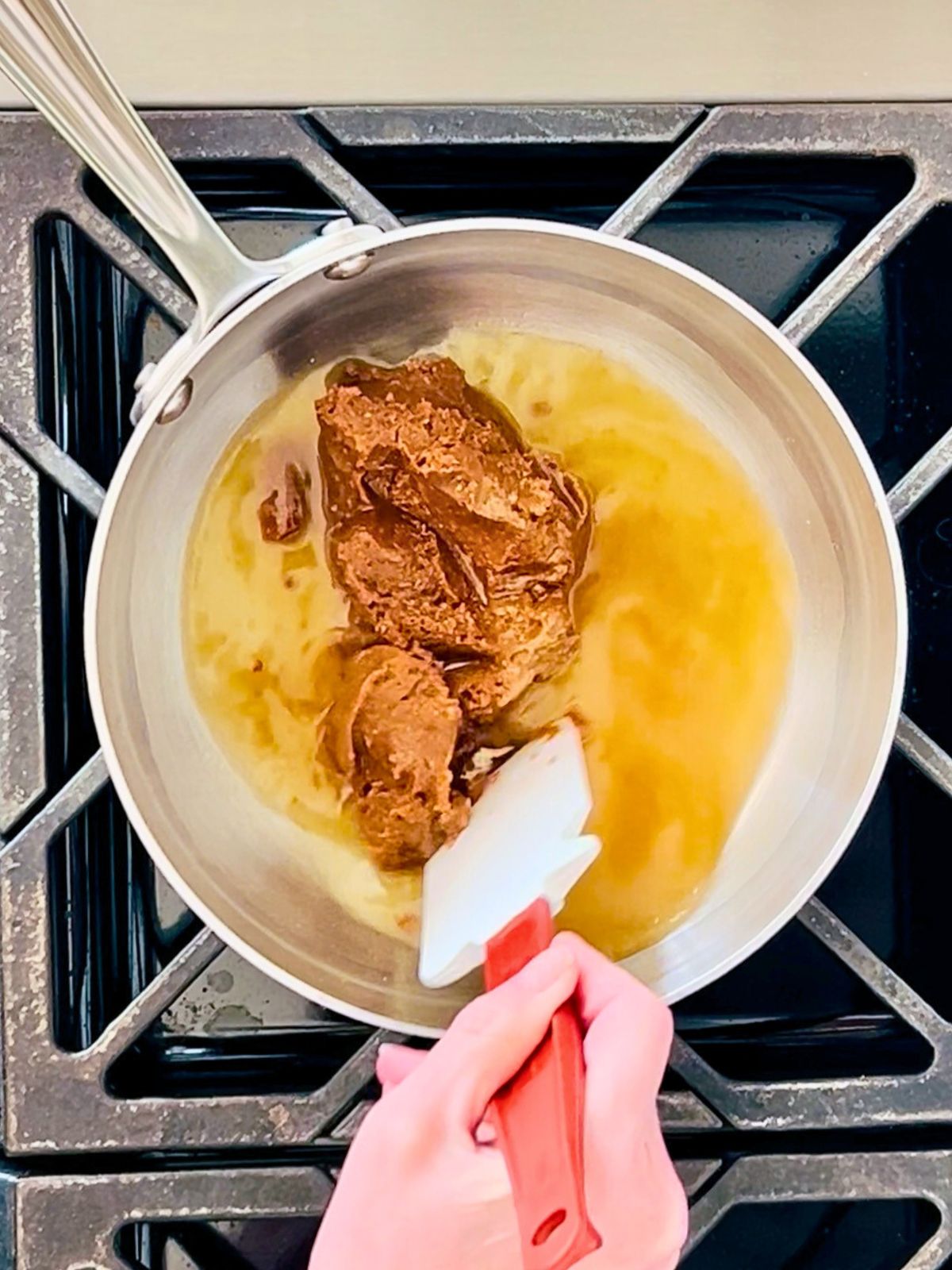 A spatula is mixing red miso paste, sugar, mirin, rice vinegar, and water in a saucepan over heat.