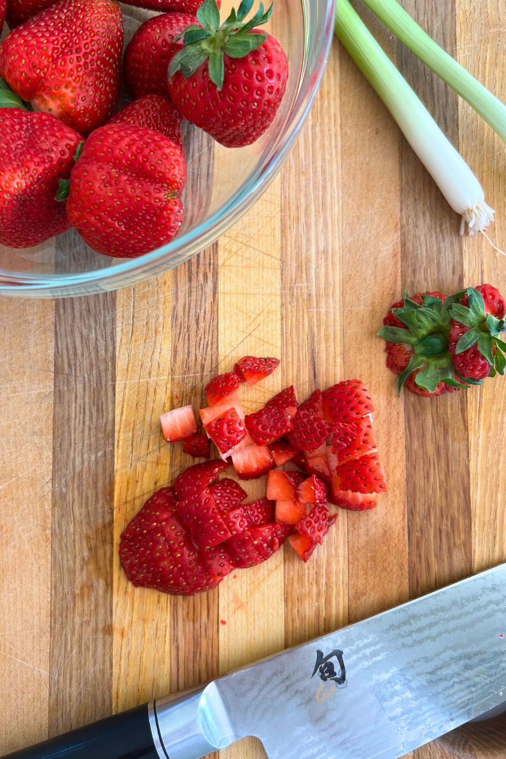 A bowl of strawberries with a few that are cut into small cubes on a cutting board for the salsa.