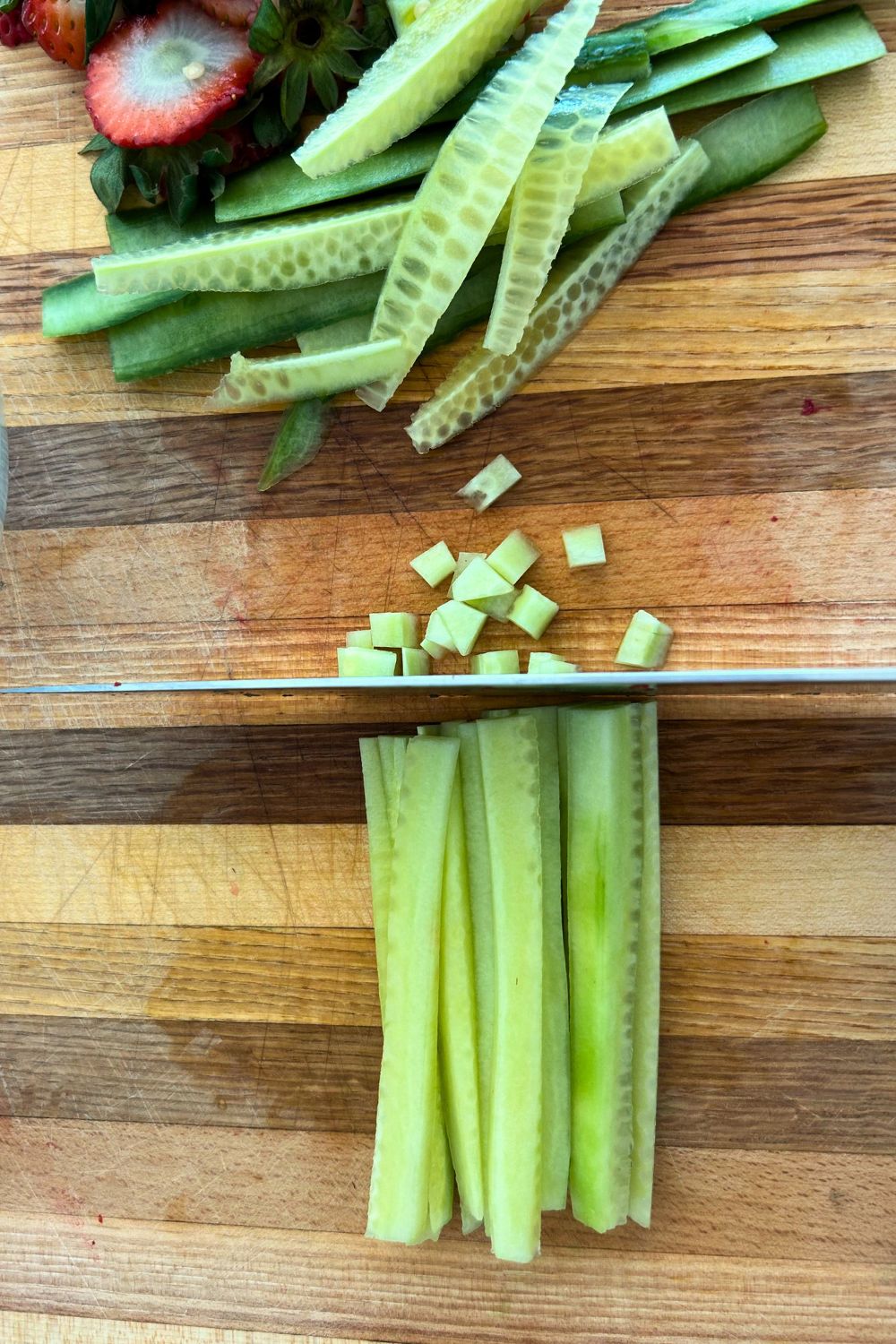 Strips of peeled and seeded cucumber are getting cut into small cubes with a knife.