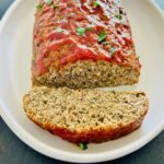 A white plate with turkey meatloaf with a sweet tangy glaze along next to one slice.