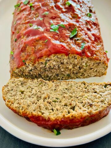 A white plate with turkey meatloaf with a sweet tangy glaze along next to one slice.