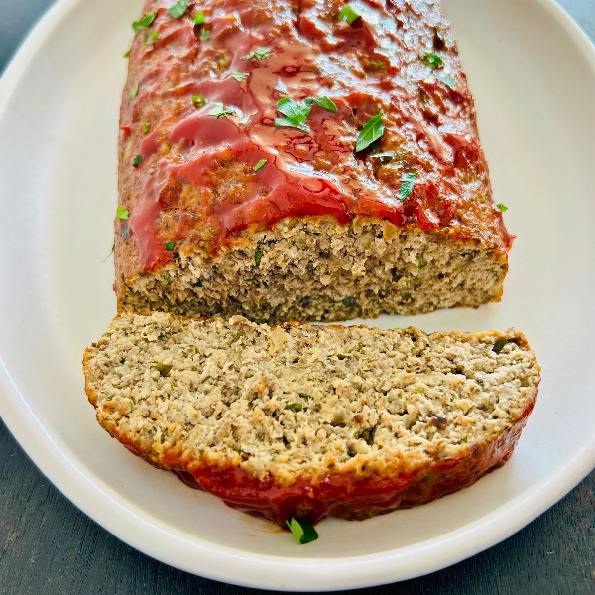 A white plate with turkey meatloaf with a sweet tangy glaze along next to one slice.