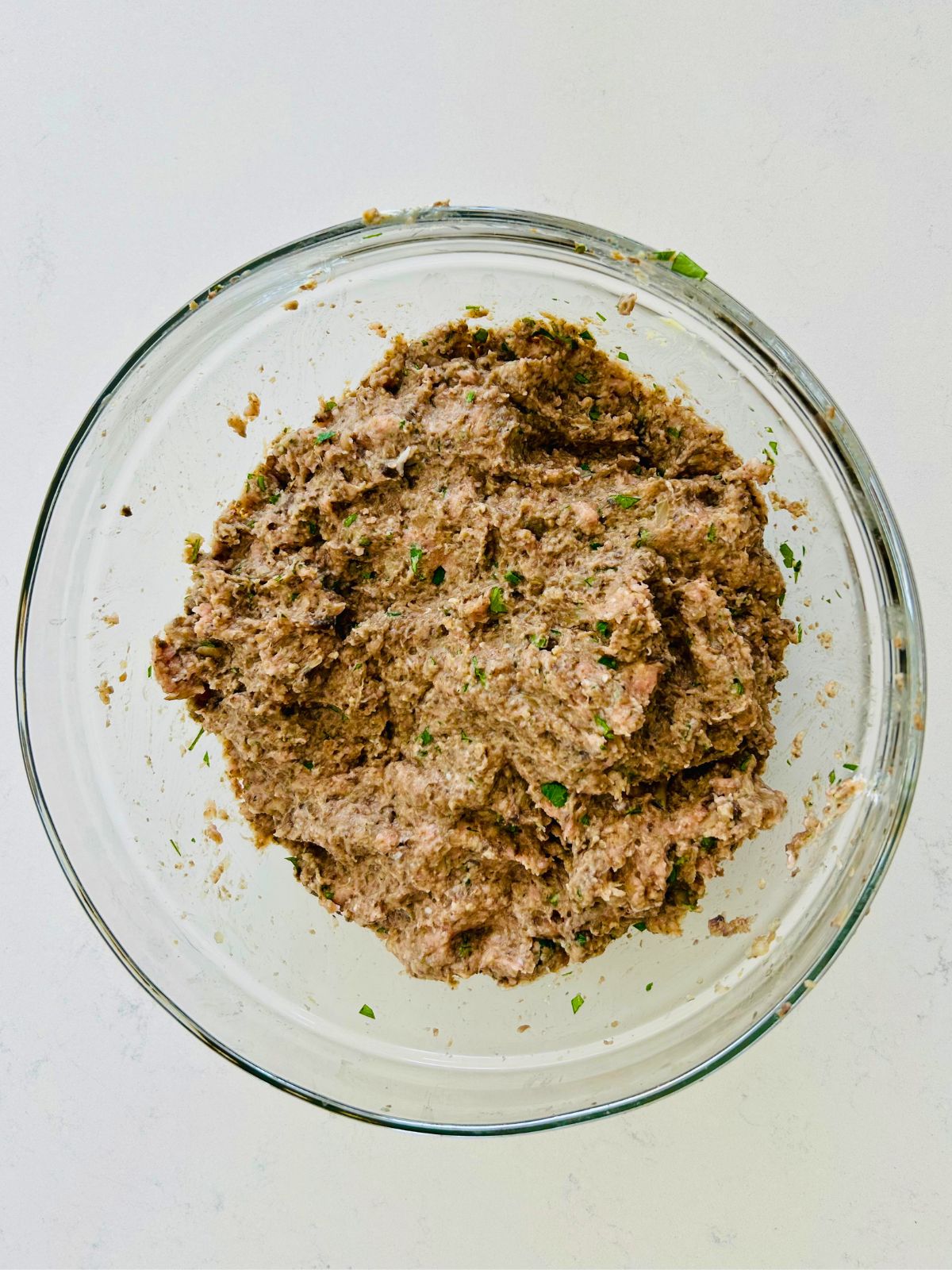 All the ingredients for a turkey meatloaf have been combined in a glass bowl.