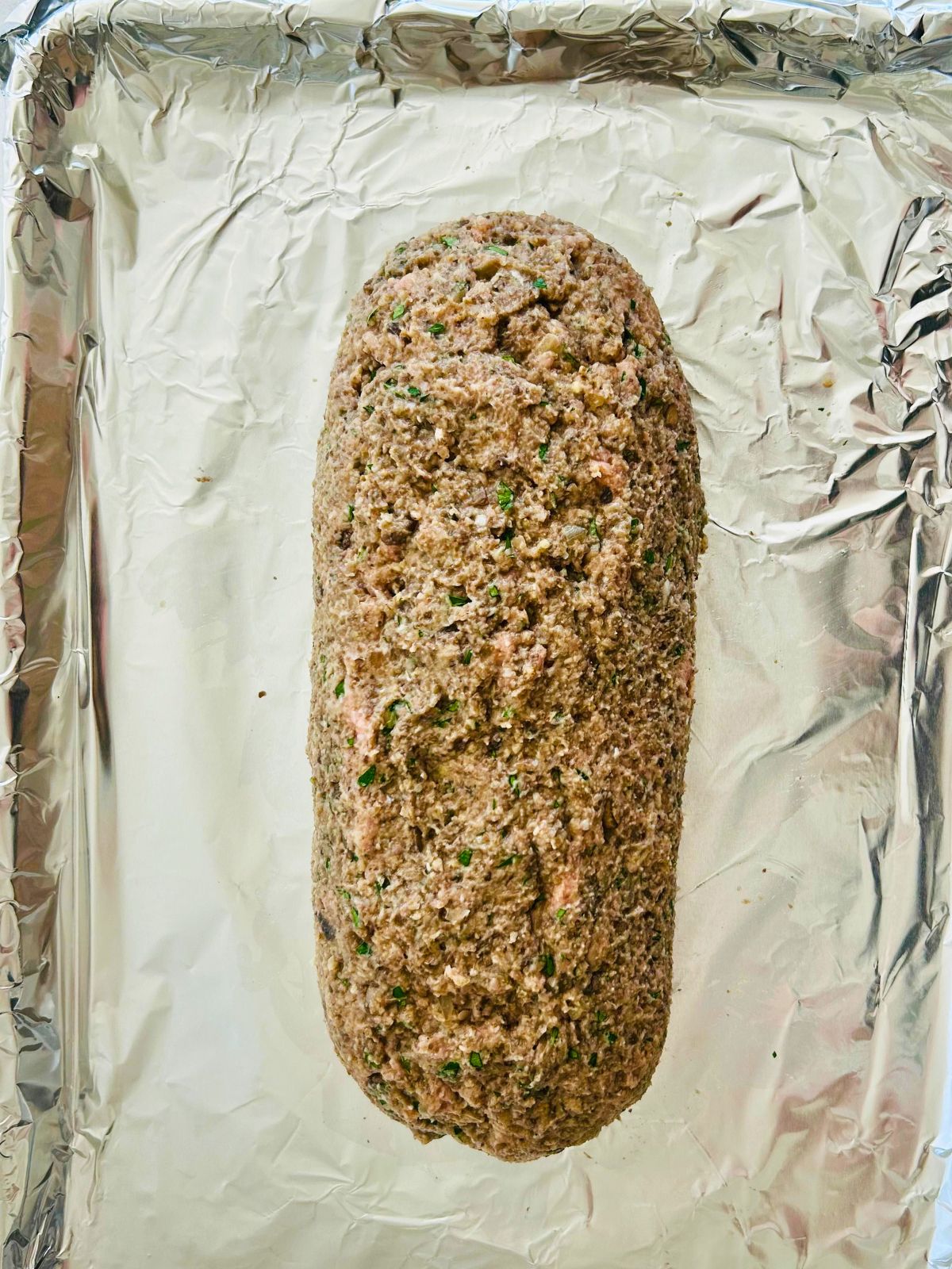 Turkey meatloaf mixture is formed into a long loaf on a foil-lined sheet pan.