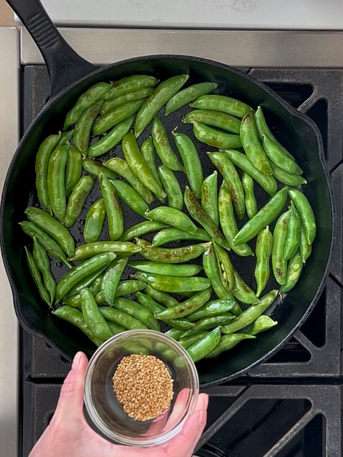 A small bowl of toasted sesame seeds will be added to a skillet of sautéed sugar snap peas.