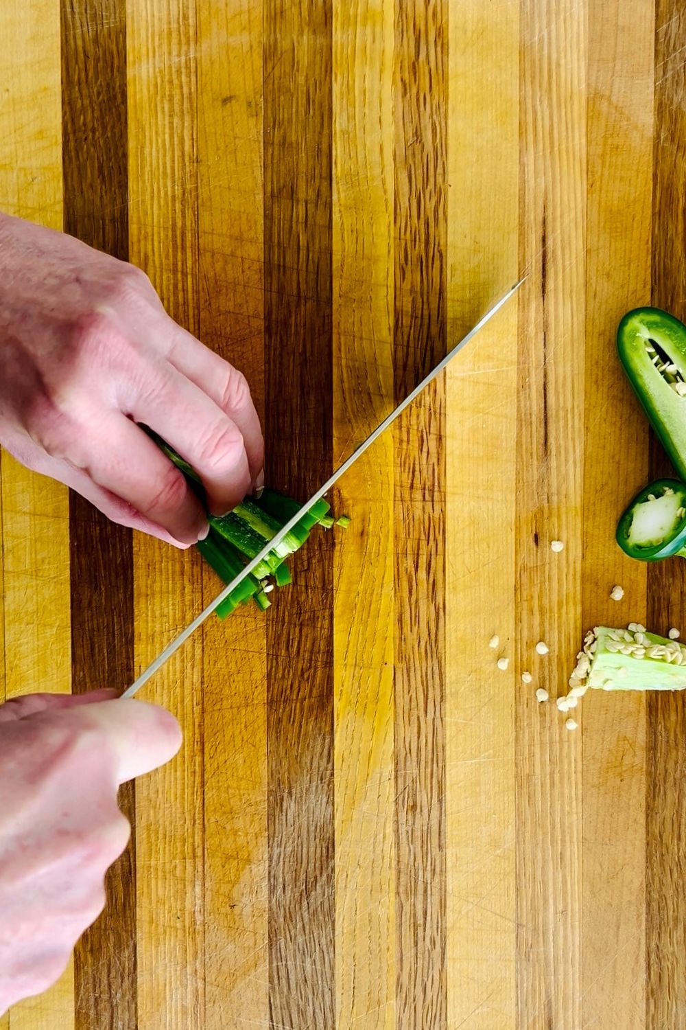 Cutting strips of jalapeno pepper into a small dice.