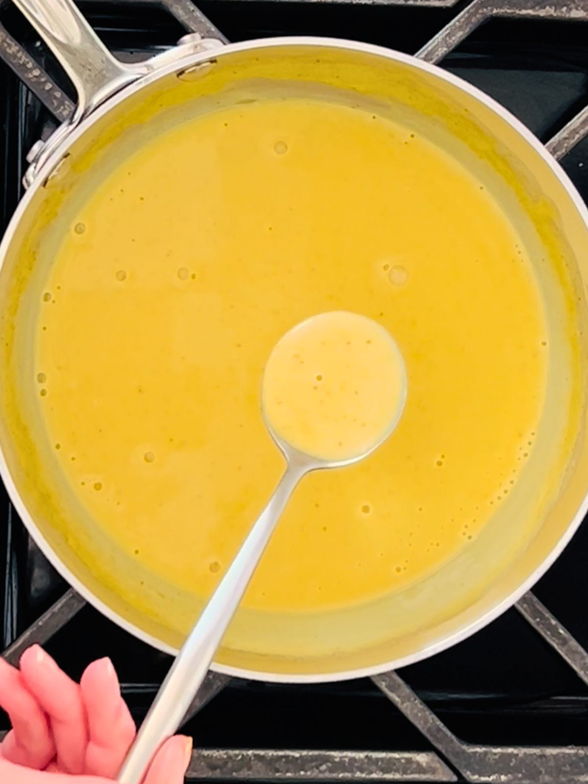 A silver spoonful of curry butter sauce over a saucepan of finished sauce.