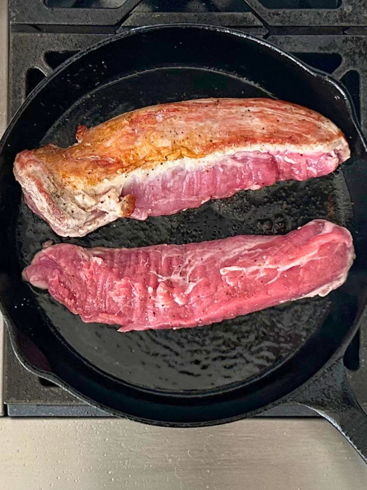 Two pork tenderloins searing in a skillet.
