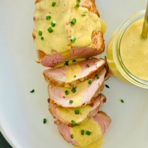 Pork tenderloin with curry butter and chives on a white platter.