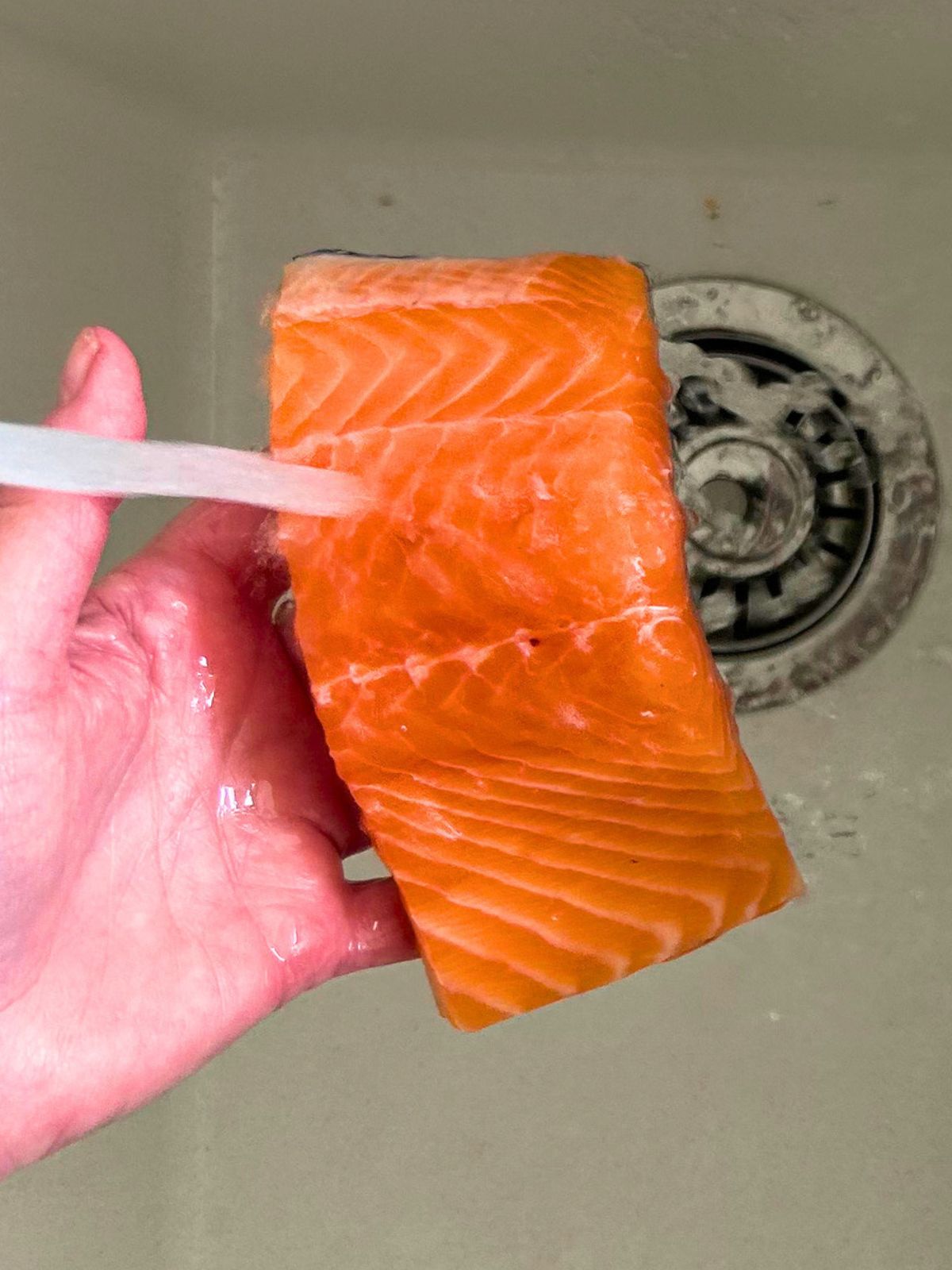Faucet water is rinsing off the dry brine from a salmon fillet.