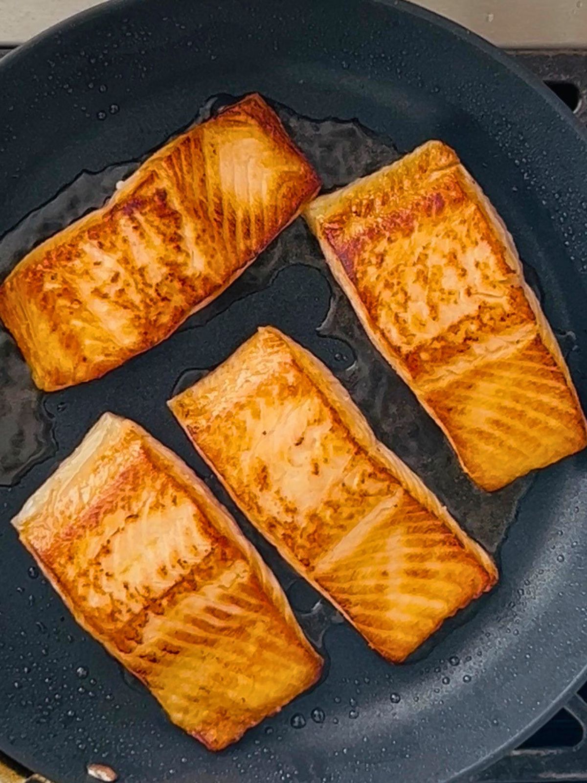 Restaurant-style seared salmon cooking in a skillet.