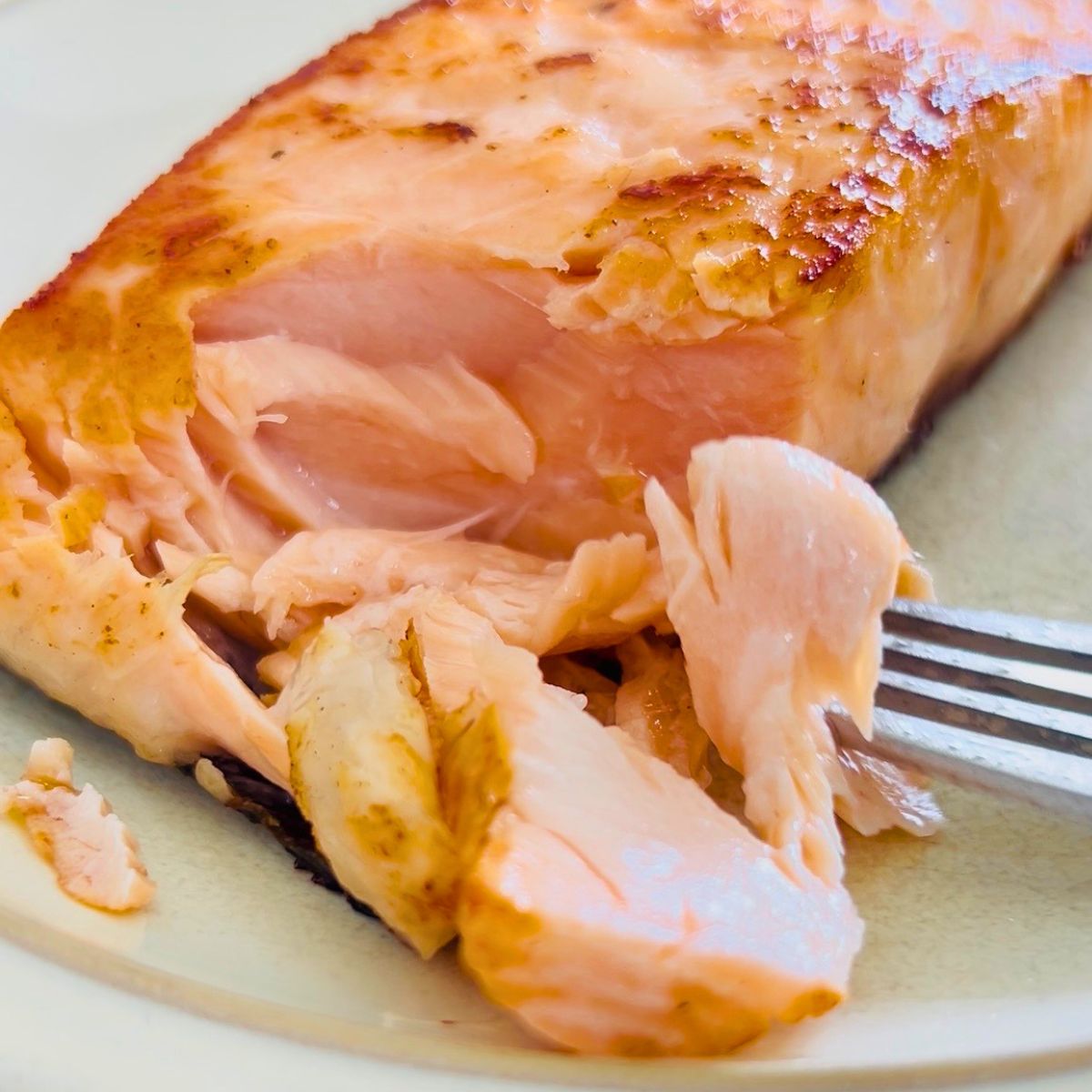 A fork is holding a partially eaten restaurant-style pan-seared salmon on a white plate.