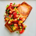 Restaurant-style pan-seared salmon on a white plate with microgreens, edible flowers, and strawberry salsa on top.