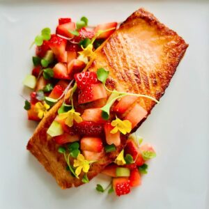 Restaurant-style pan-seared salmon on a white plate with microgreens, edible flowers, and strawberry salsa on top.