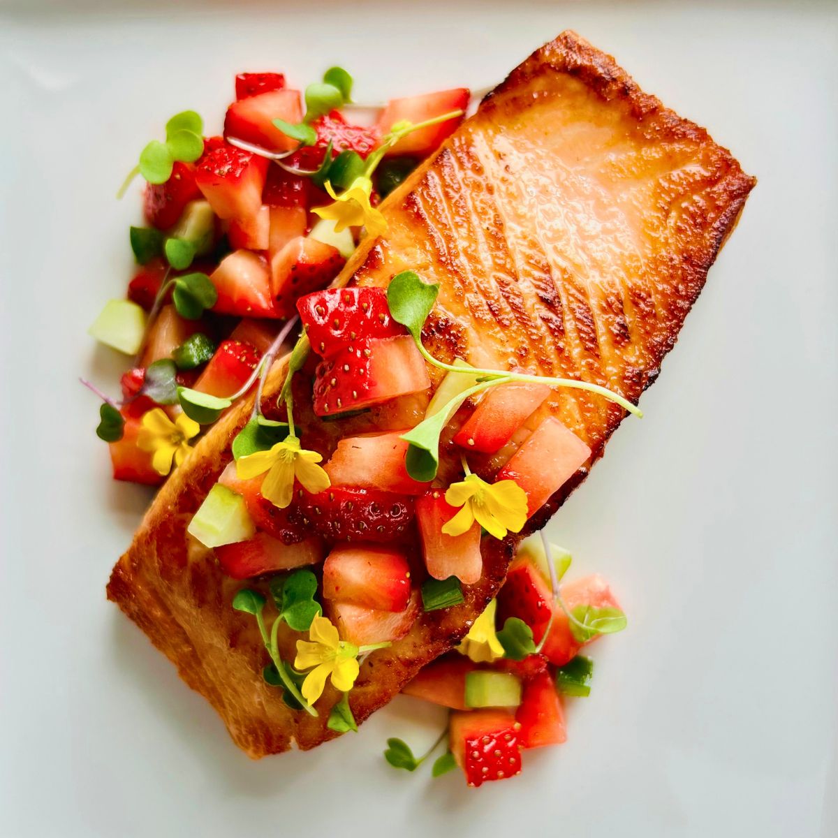 Restaurant-style pan-seared salmon on a white plate with microgreens, edible flowers, and strawberry salsa on top.