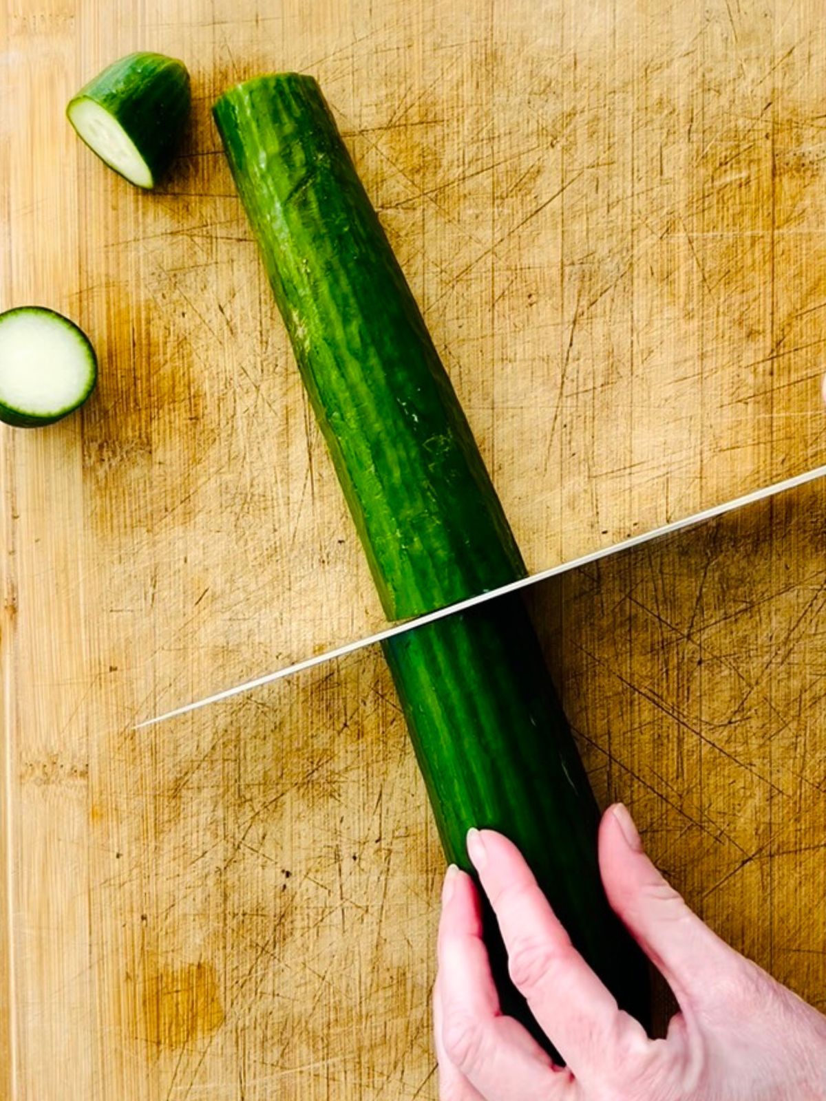 Trimming the ends of an English cucumber on a wooden cutting board before spiralizing into cucumber noodles.