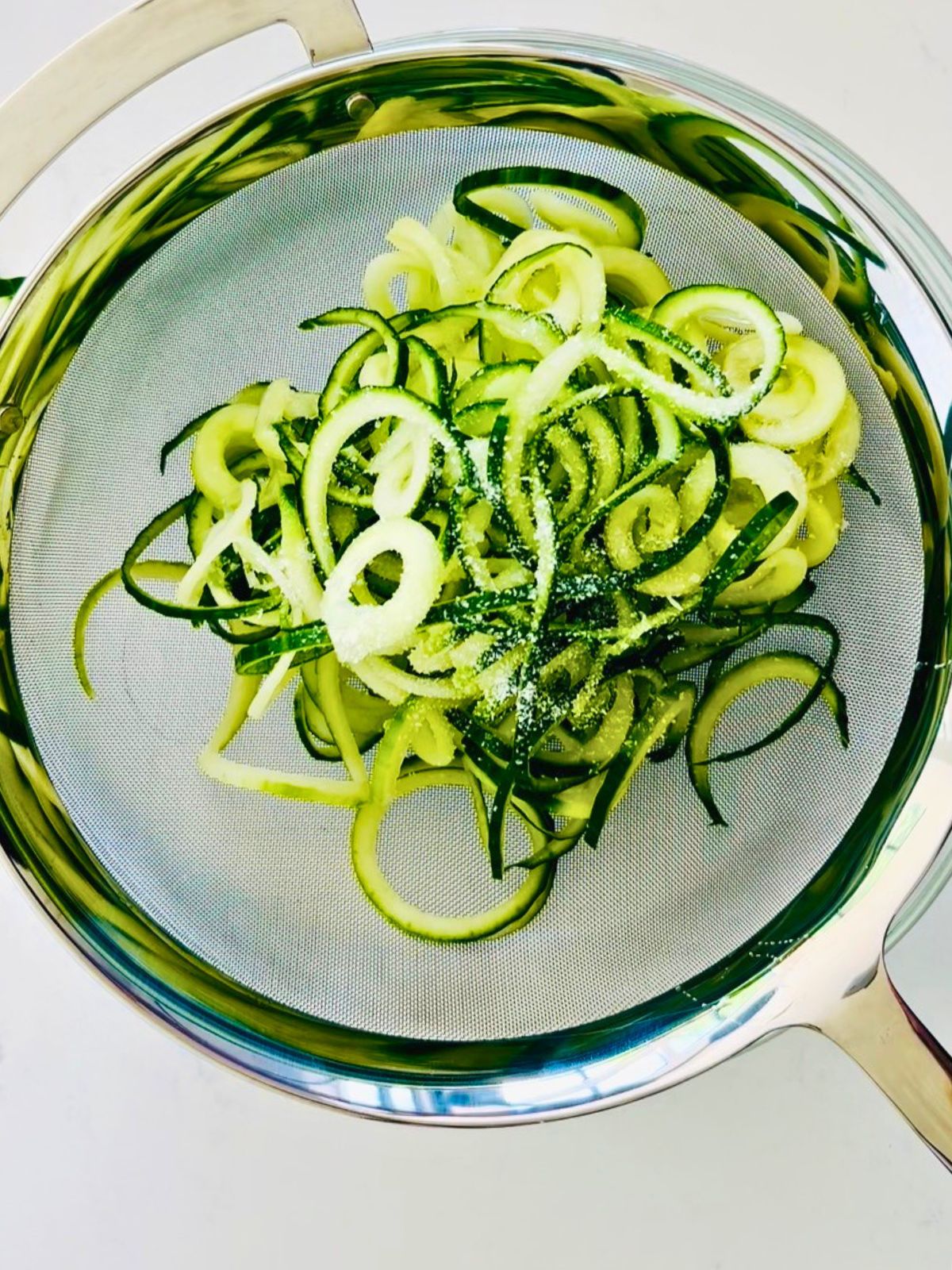 Spiralized cucumber noodles salted and draining in a fine mesh strainer to remove excess moisture before dressing.