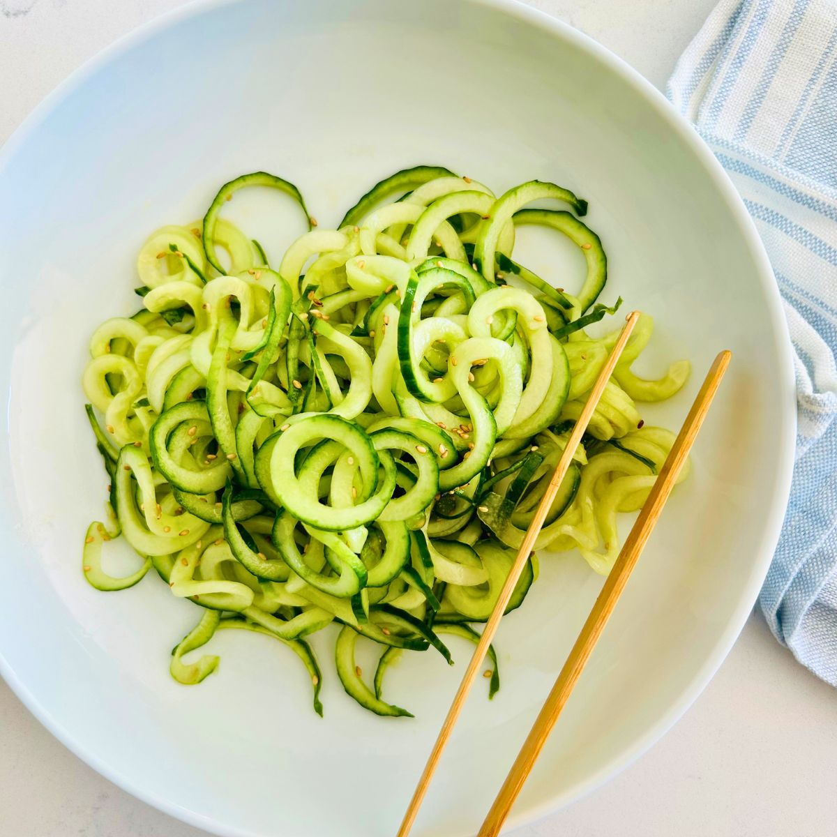 Spiralized cucumber noodles in a white bowl with chop sticks resting on the side.