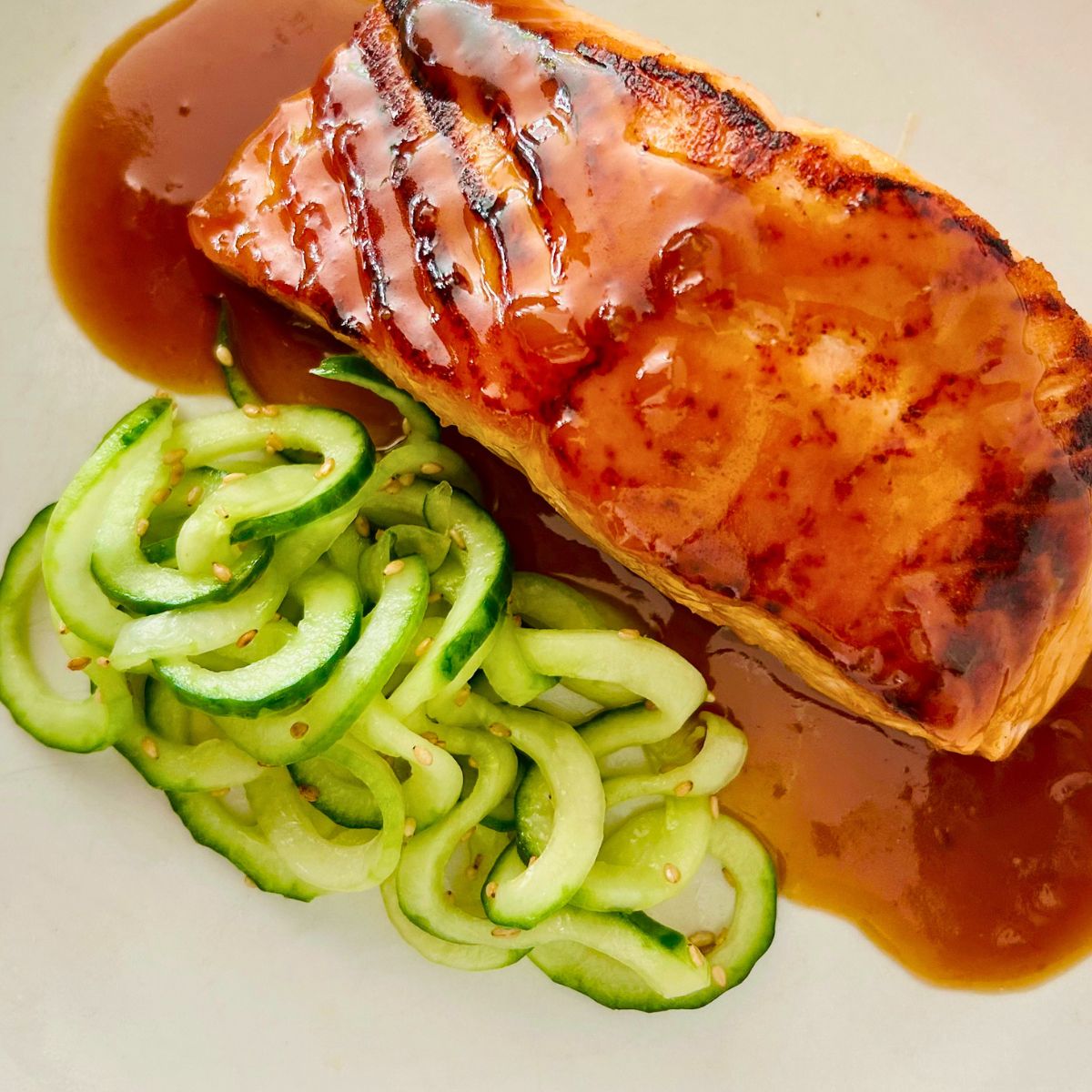 A white plate of cucumber noodles, pan-seared salmon, and miso butter sauce.