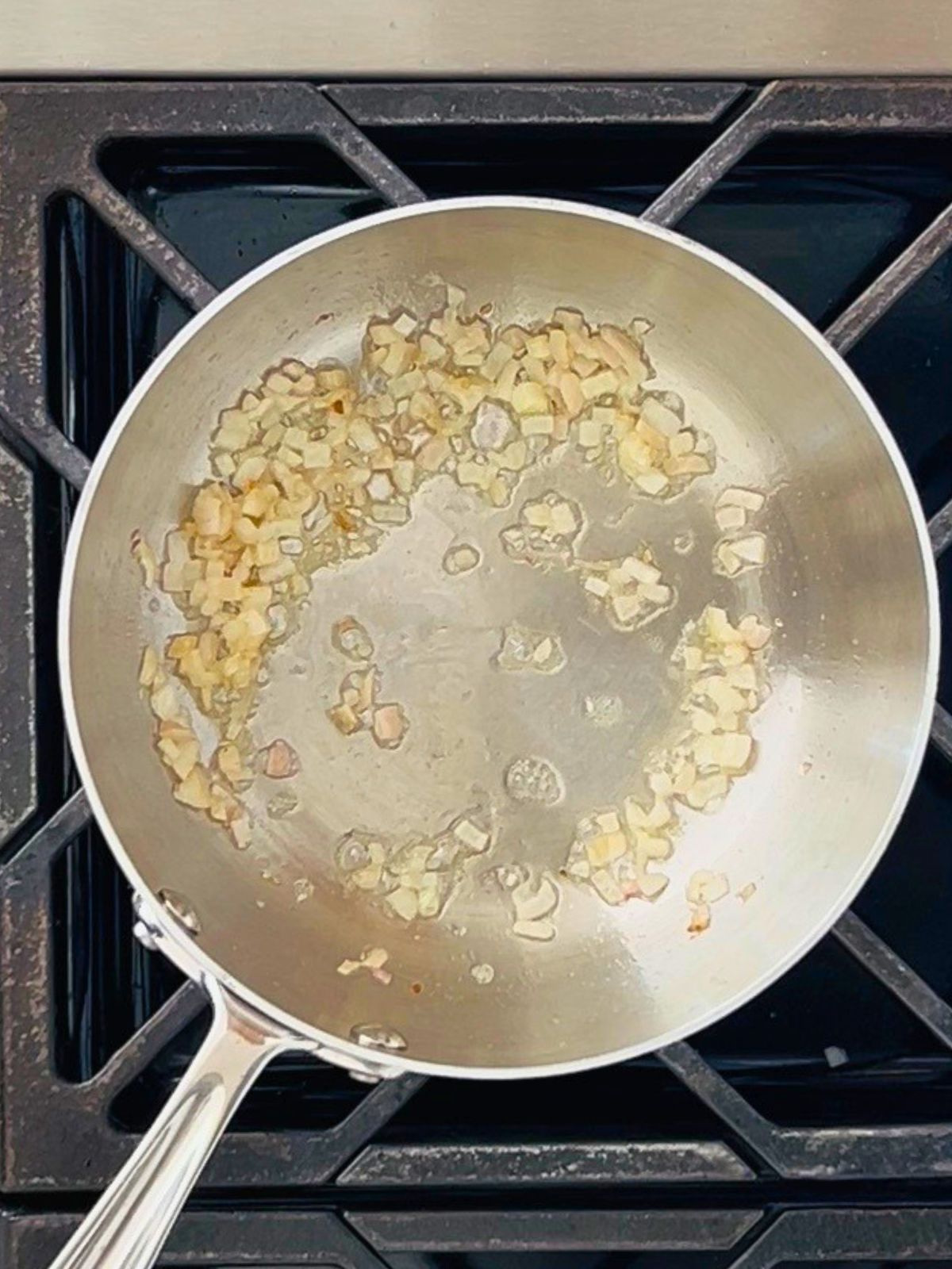 Sautéed minced shallots in a stainless steel sauce pan on a gas stovetop.