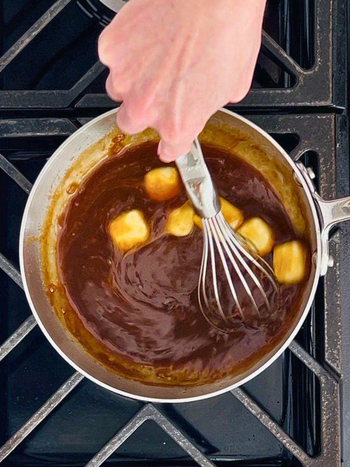 Whisking cold butter cubes into miso butter sauce reduction in a skillet.
