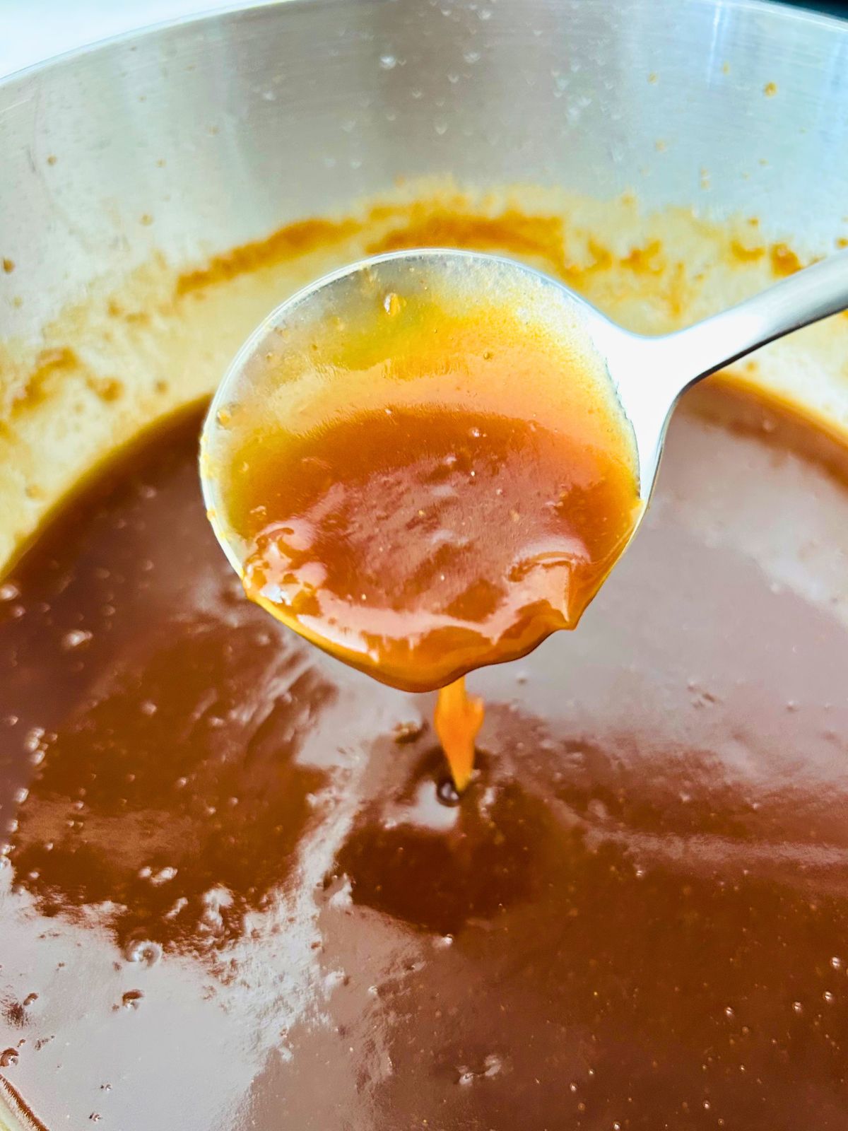 Spoonful of finished miso butter sauce dripping from a ladle showing the silky emulsified texture.