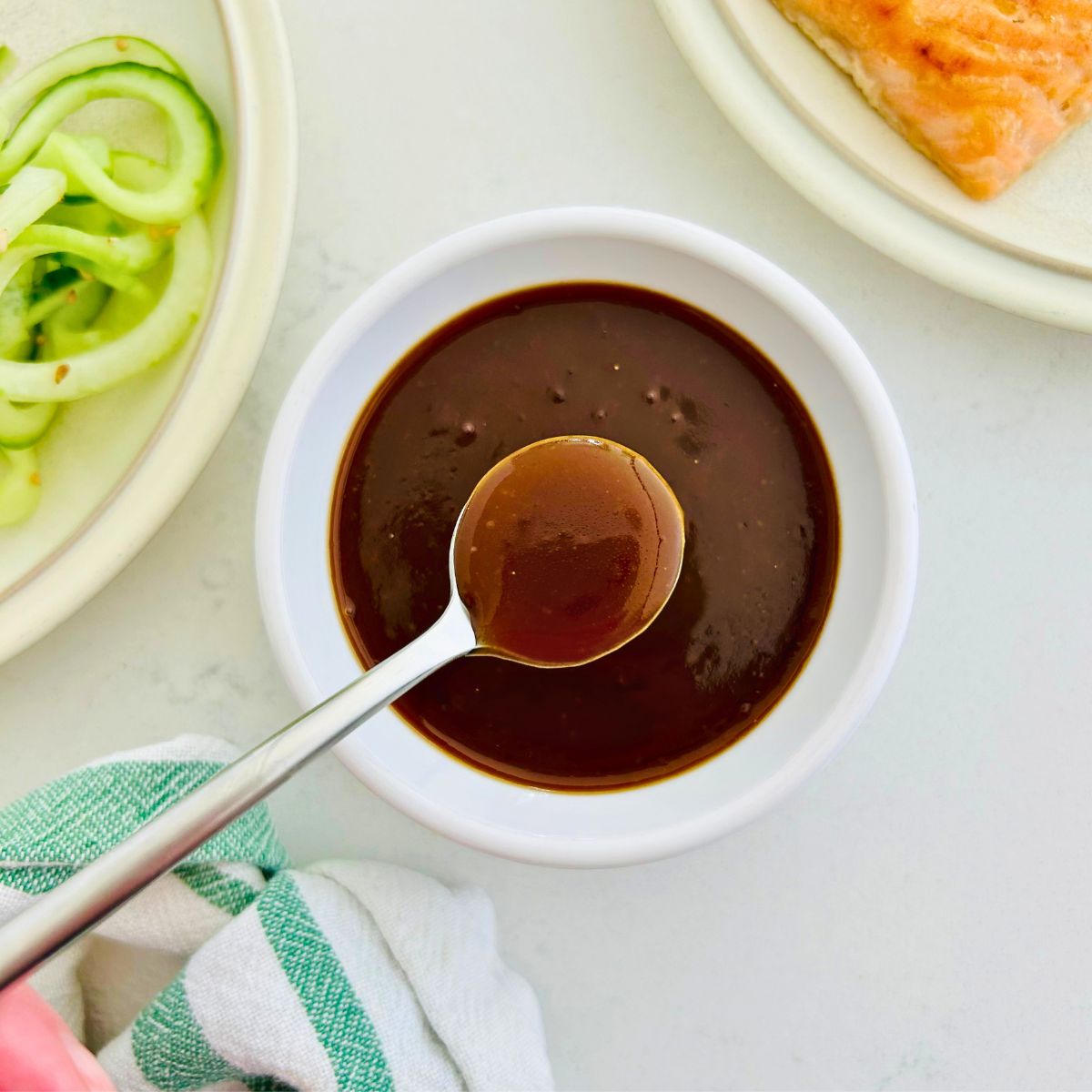 A spoon of miso butter sauce held over a small white bowl of sauce.