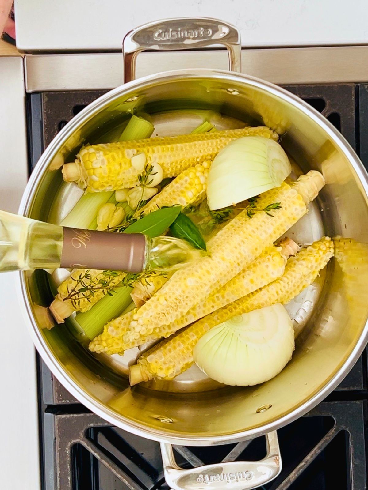 Pouring white wine over corn cobs, leeks, onion, and herbs in a stockpot for corn stock recipe.