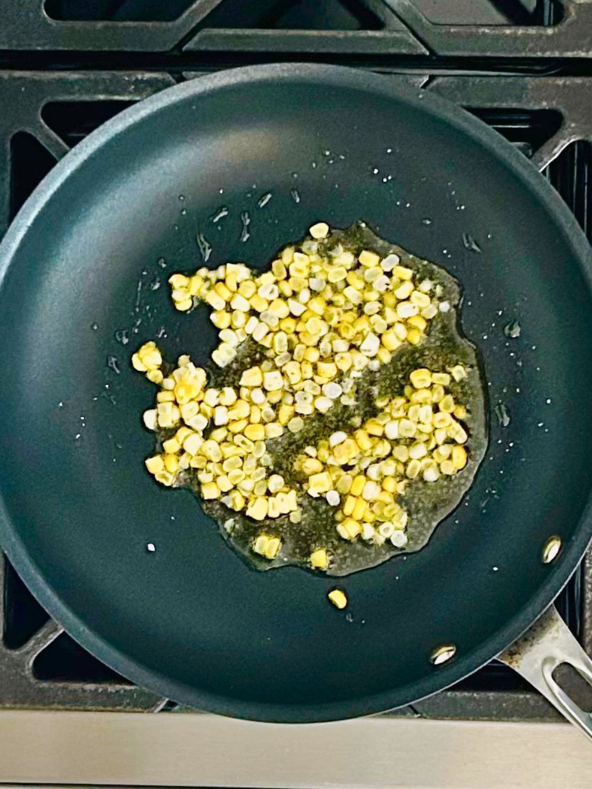 Freshly cut corn kernels are cooking in a skillet with olive oil.