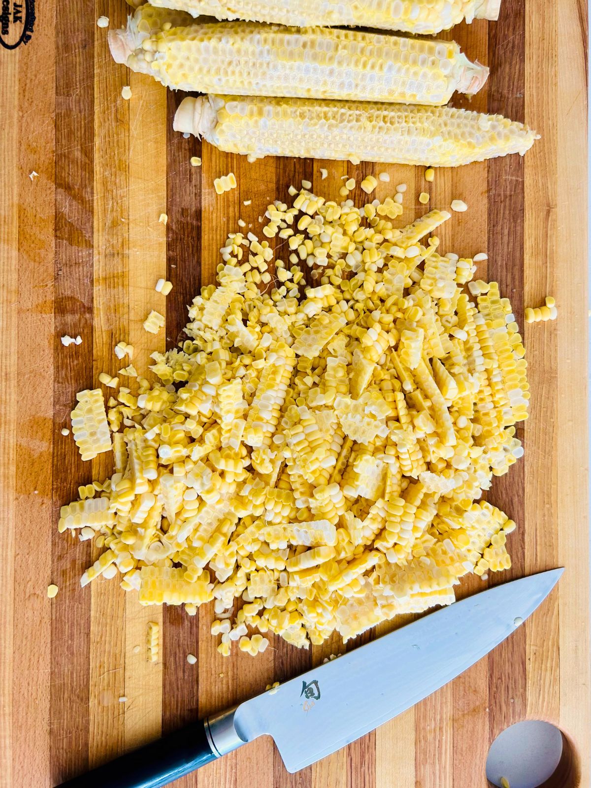 Corn kernels on a cutting board have been cut off the corn cobs.