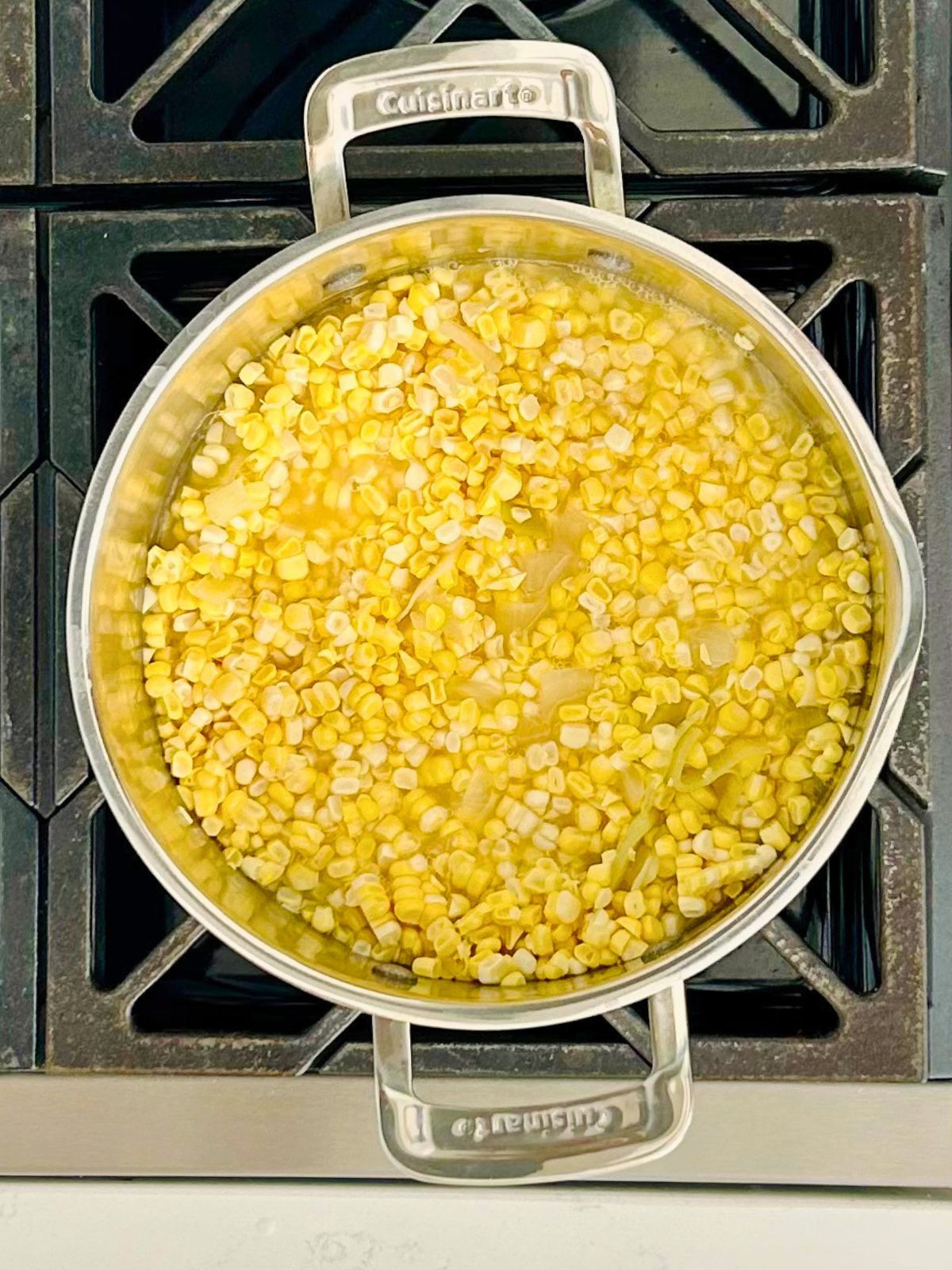 Fresh corn kernels are simmering in a pot of cooked vegetables for corn soup.