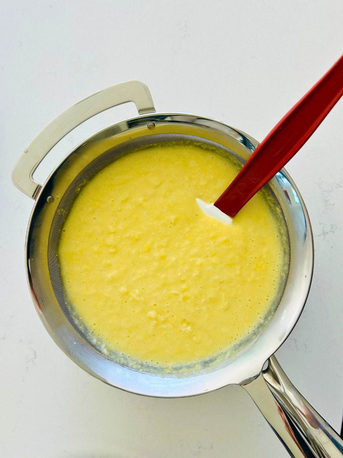 Blended corn soup in a strainer resting over a pot to remove the solid bits.