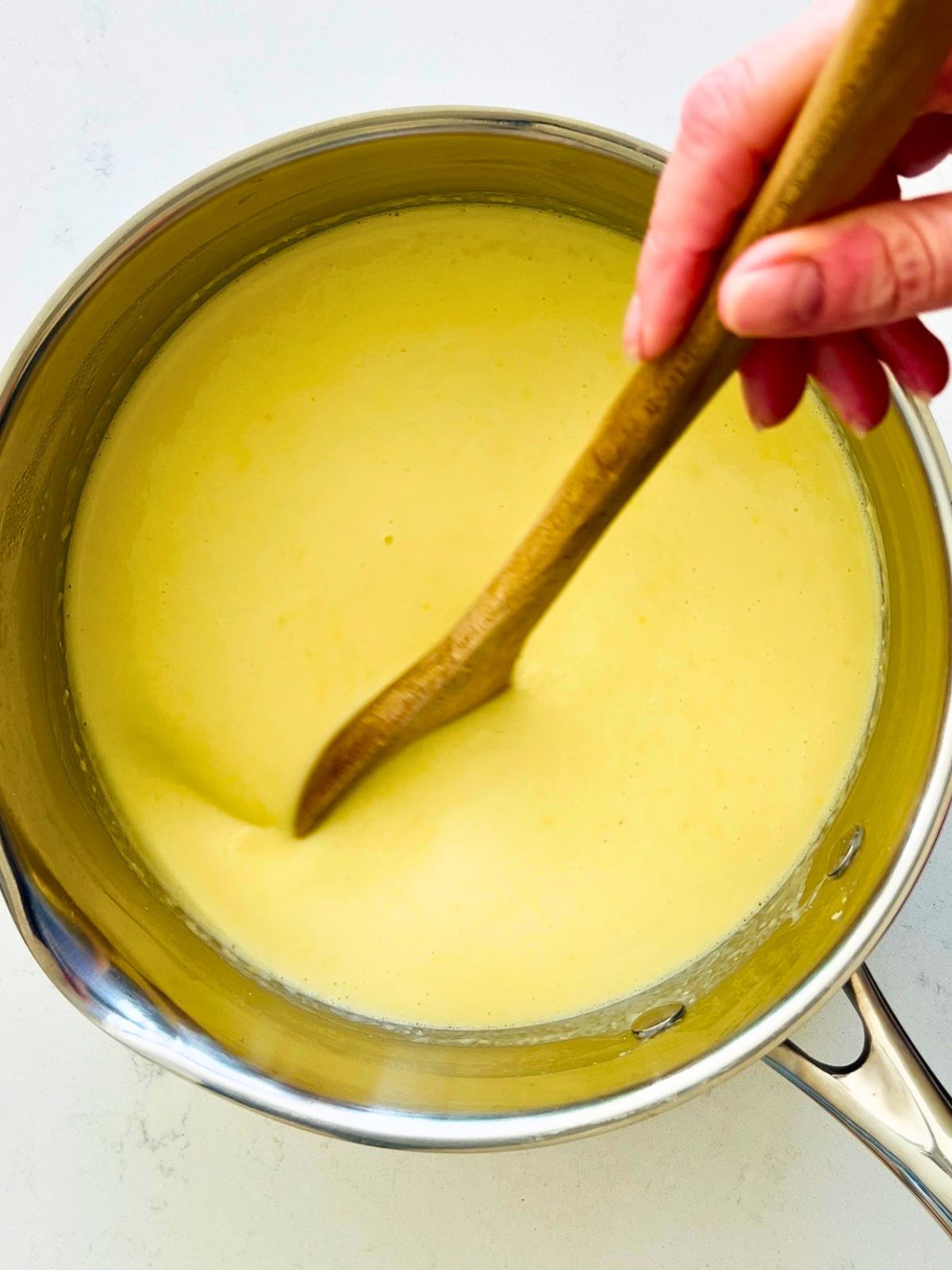 A wooden spoon is stirring the creamy corn soup in a pot.