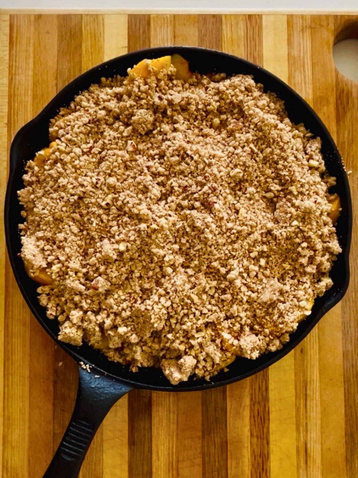 Peach crisp with pecans assembled in a cast iron skillet before baking.
