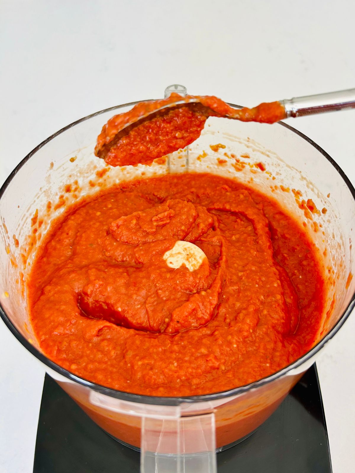 Smooth, deep red homemade tomato paste with a spoonful held upside down over a food processor bowl.