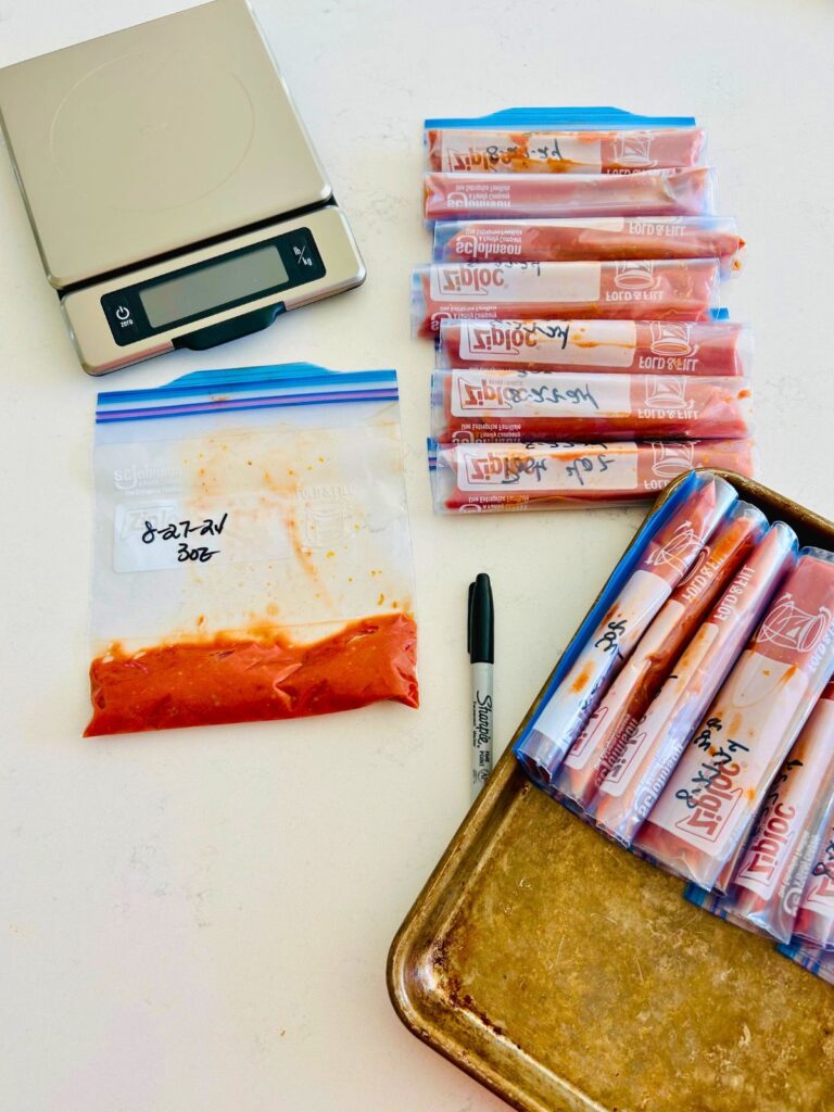 Tomato paste is portioned into freezer bags by weight alongside a kitchen scale and Sharpie.